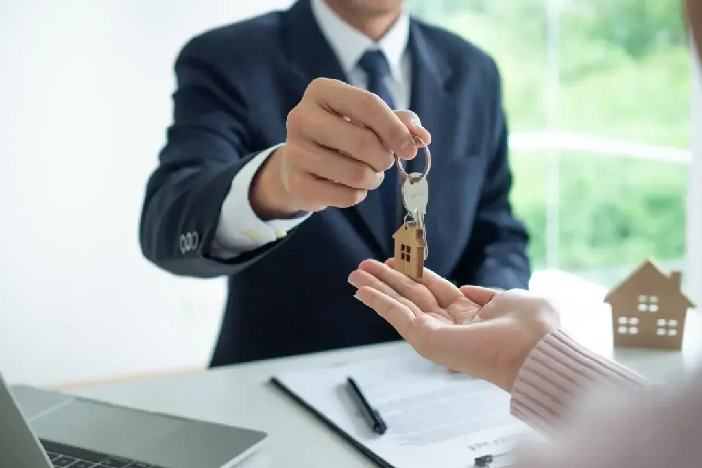 Agente imobiliário entrega chaves de casa a comprador, simbolizando contrato de crédito habitação com beneficiário irrevogável.
