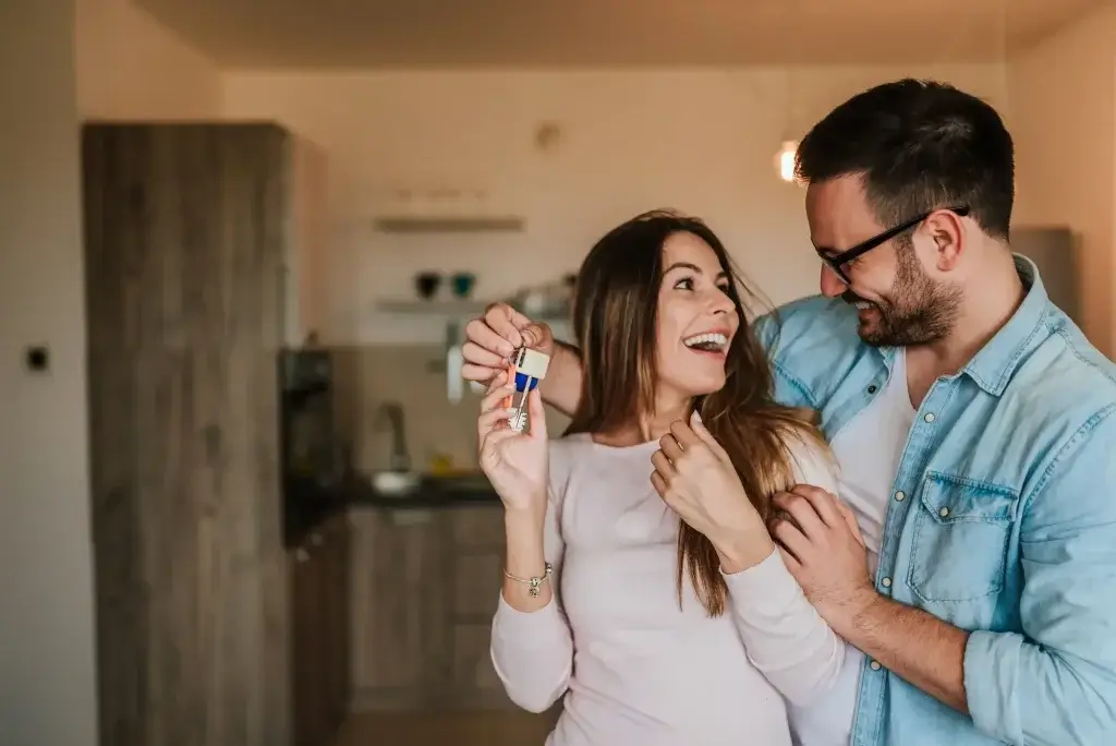 Casal feliz em casa nova a segurar as chaves, representando a tranquilidade de quem escolheu o melhor seguro vida crédito habitação.